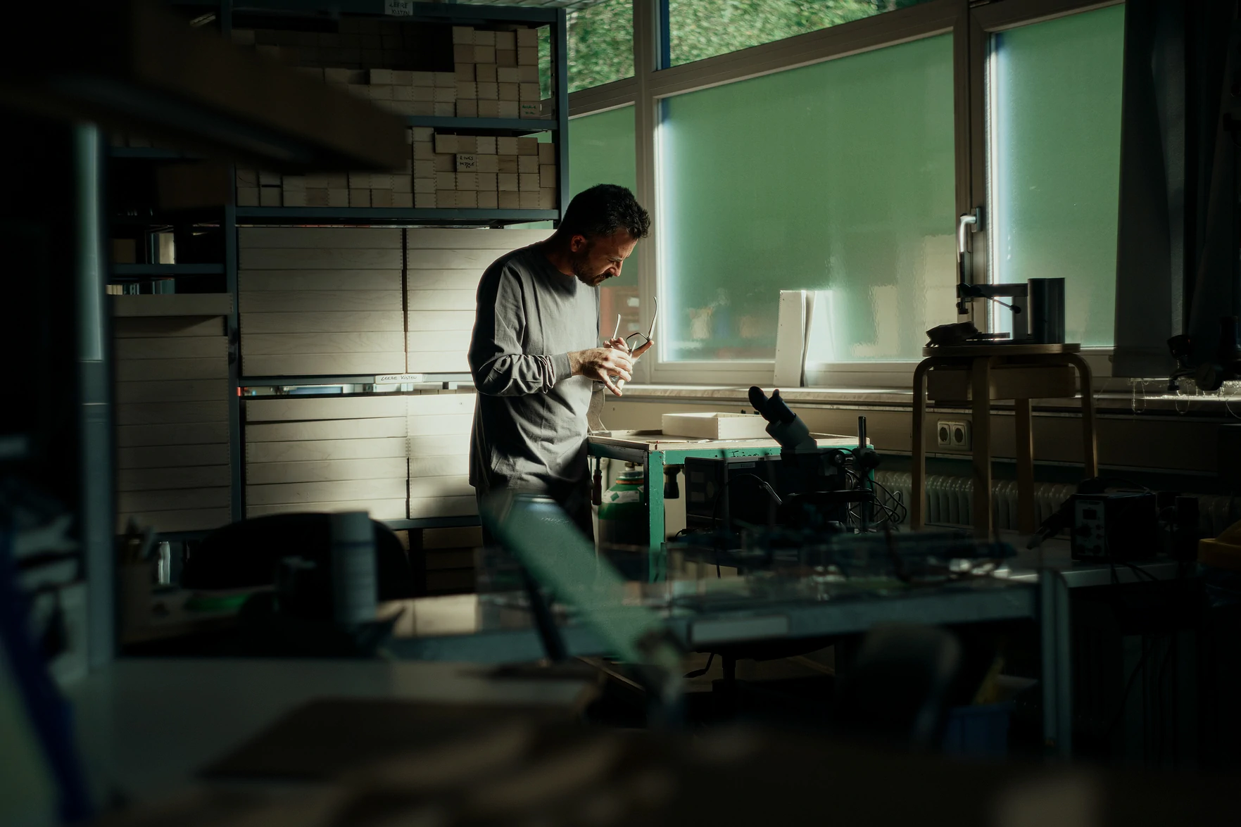 Artisan lunetier contrôlant une monture à la lumière de la fenêtre dans un atelier de fabrication de lunettes